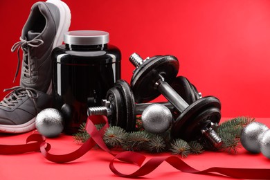 Photo of Dumbbells, container with supplement, sneakers and Christmas decor on red background