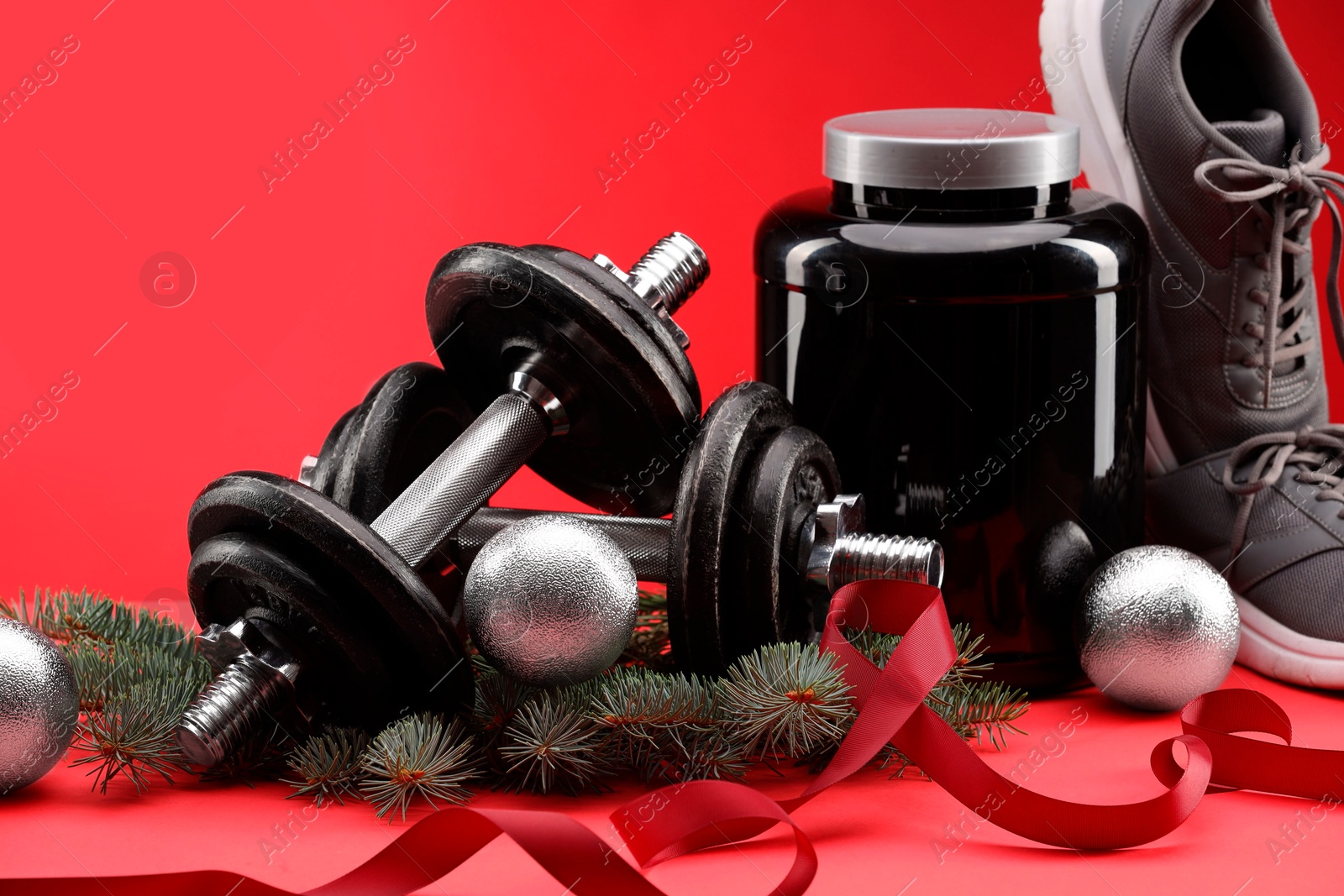 Photo of Dumbbells, container with supplement, sneakers and Christmas decor on red background