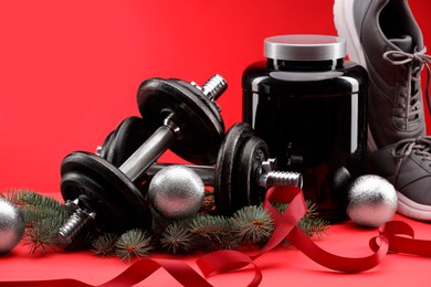 Photo of Dumbbells, container with supplement, sneakers and Christmas decor on red background