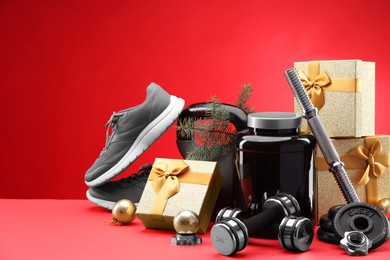 Photo of Dumbbells, kettlebell, container with supplement, sneakers and Christmas decor on red background. Space for text