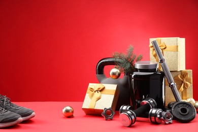 Photo of Dumbbells, kettlebell, container with supplement, sneakers and Christmas decor on red background. Space for text