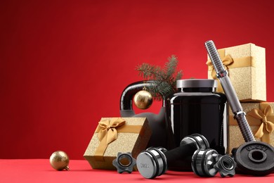 Photo of Dumbbells, kettlebell, container with supplement and Christmas decor on red background. Space for text