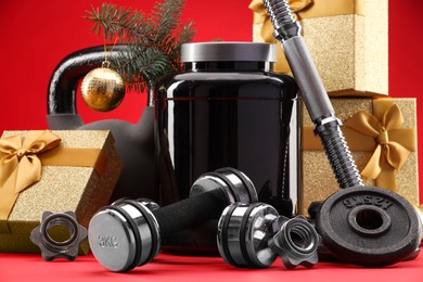 Photo of Dumbbells, kettlebell, container with supplement and Christmas decor on red background