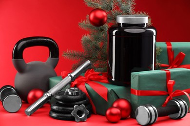 Photo of Dumbbells, kettlebell, container with supplement and Christmas decor on red background