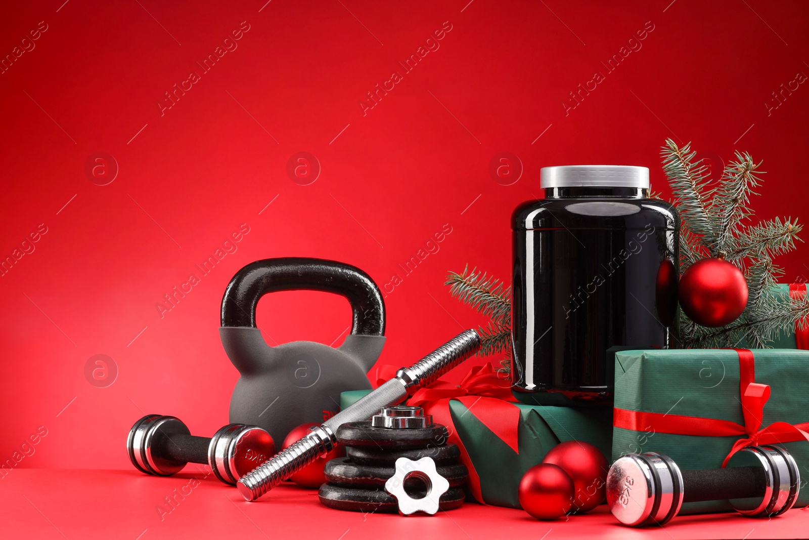 Photo of Dumbbells, kettlebell, container with supplement and Christmas decor on red background. Space for text