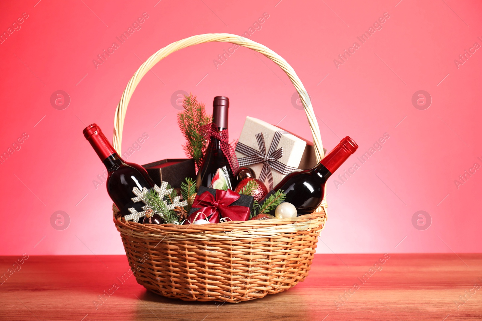 Photo of Wicker gift basket with wine on wooden table against pink background