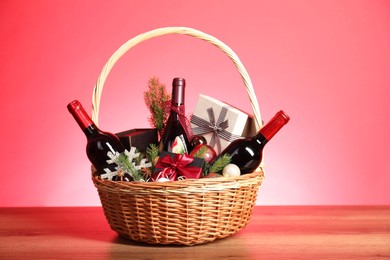 Photo of Wicker gift basket with wine on wooden table against pink background