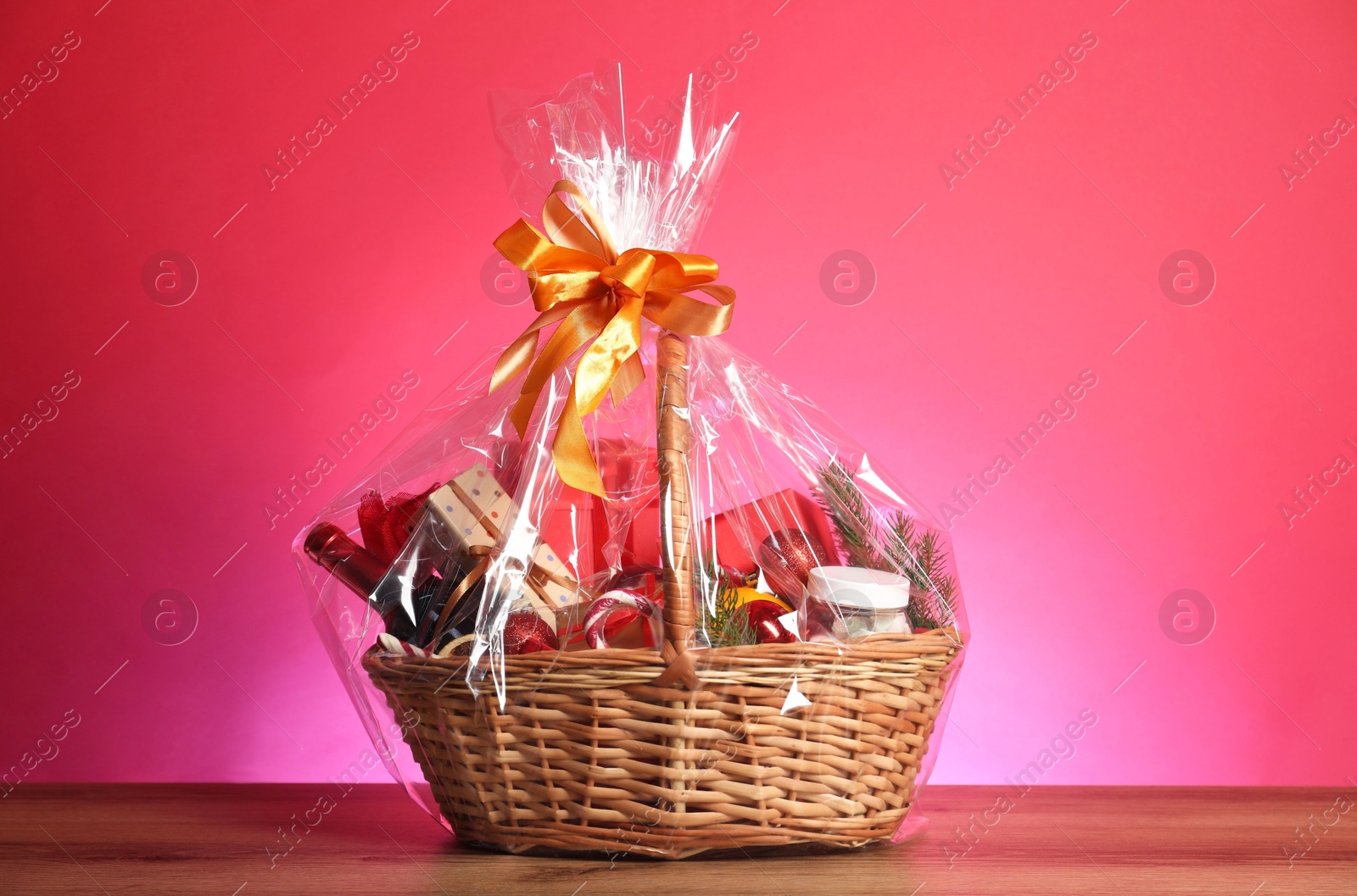 Photo of Wicker gift basket with wine on wooden table against pink background