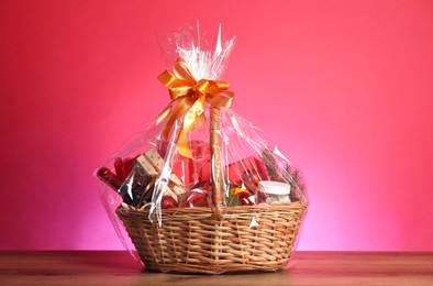 Photo of Wicker gift basket with wine on wooden table against pink background