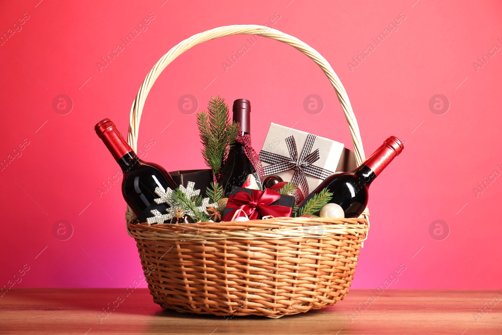 Photo of Wicker gift basket with wine on wooden table against pink background