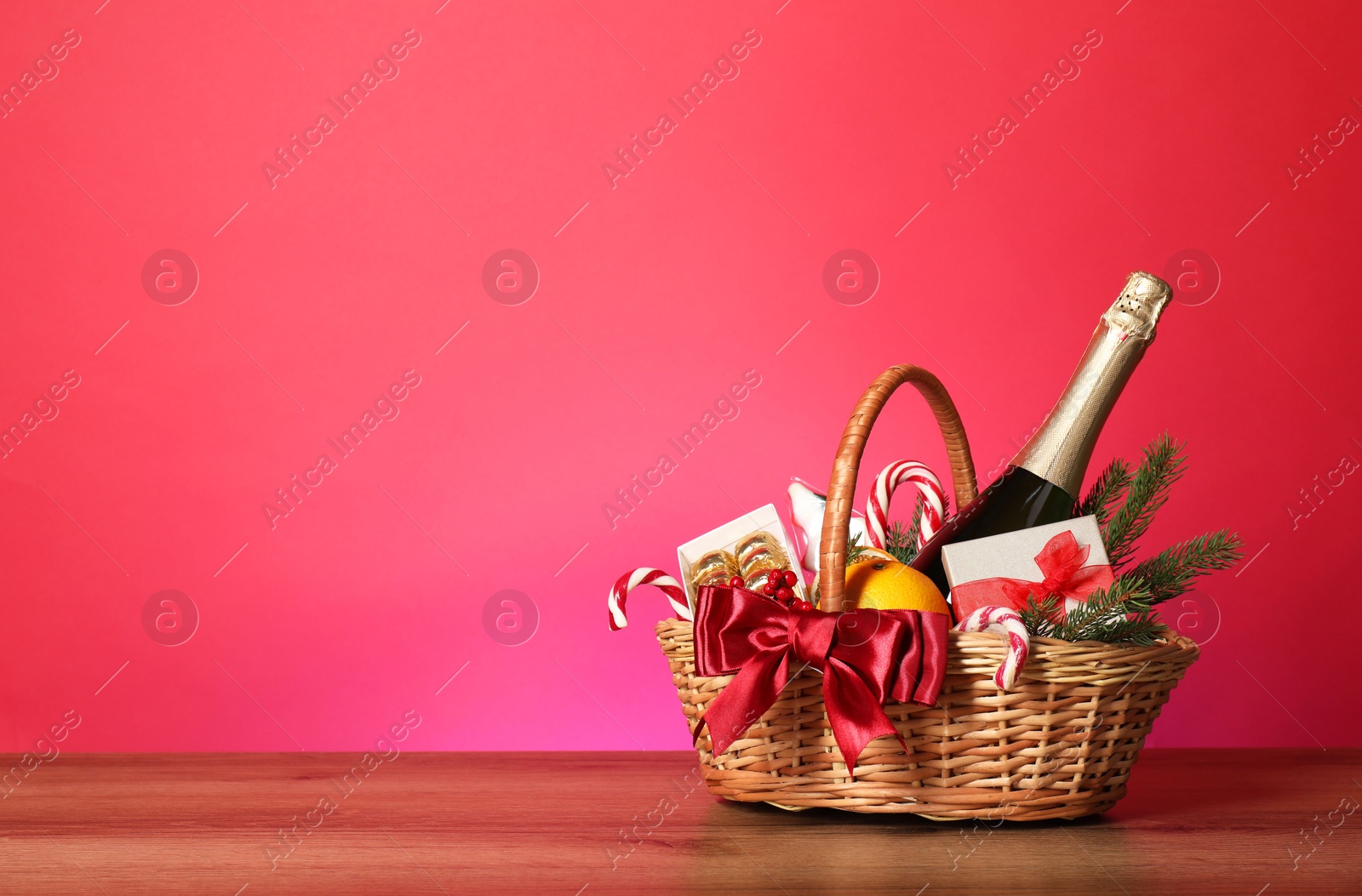 Photo of Wicker gift basket with wine on wooden table against pink background, space for text