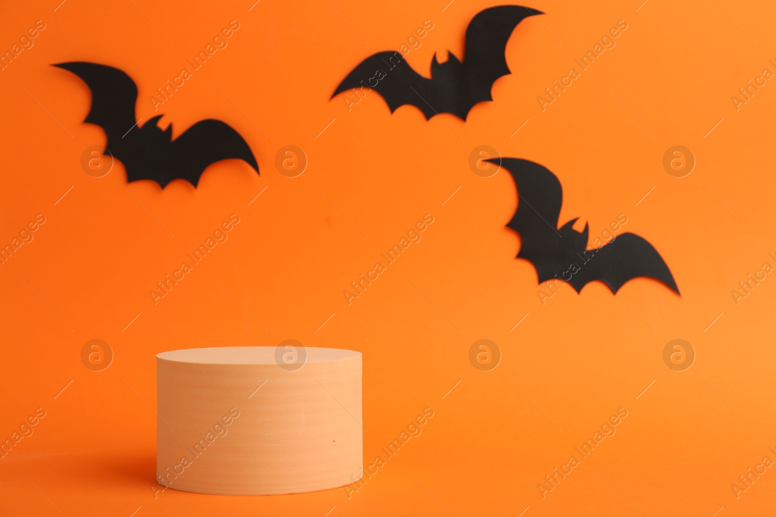 Photo of Halloween celebration. Black paper bats and podium on orange background