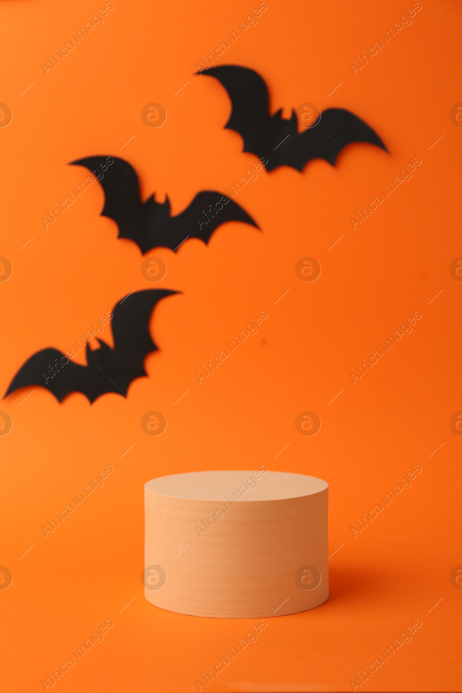 Photo of Halloween celebration. Black paper bats and podium on orange background