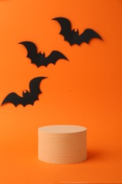 Halloween celebration. Black paper bats and podium on orange background