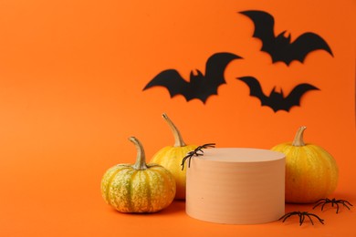 Photo of Halloween celebration. Black paper bats, spiders pumpkins and podium on orange background, space for text