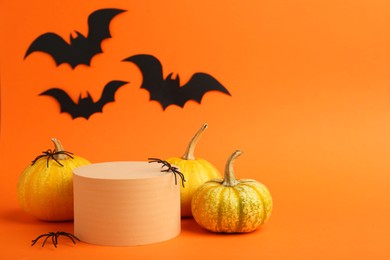 Photo of Halloween celebration. Black paper bats, spiders pumpkins and podium on orange background, space for text