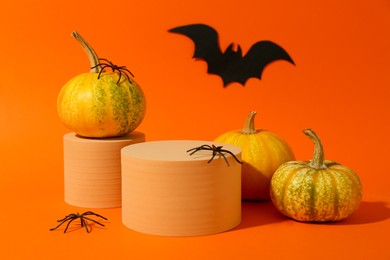 Photo of Halloween celebration. Pumpkins, black paper bat, spiders and podiums on orange background