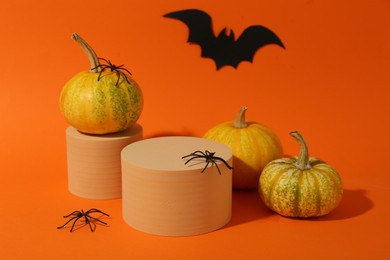 Photo of Halloween celebration. Pumpkins, black paper bat, spiders and podiums on orange background