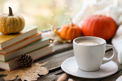 Photo of Cup of coffee, books and autumn decor on wooden table, closeup