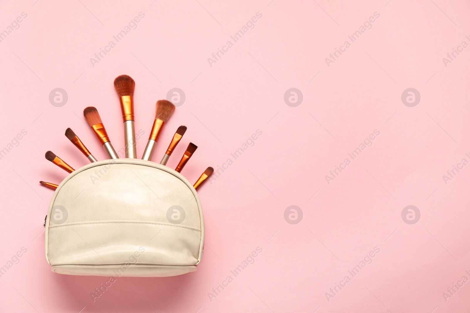 Photo of Cosmetic bag with makeup brushes on pink background, top view. Space for text