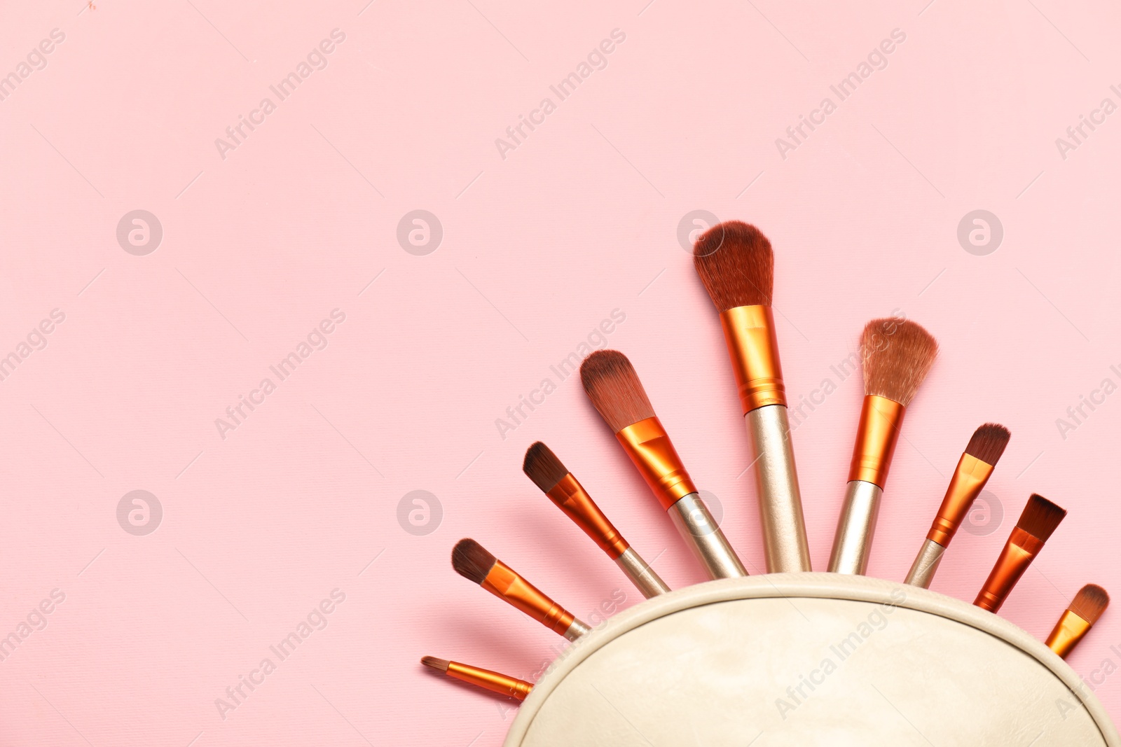 Photo of Cosmetic bag with makeup brushes on pink background, top view. Space for text