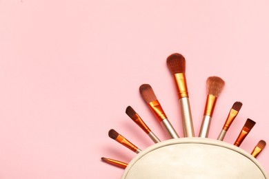 Photo of Cosmetic bag with makeup brushes on pink background, top view. Space for text