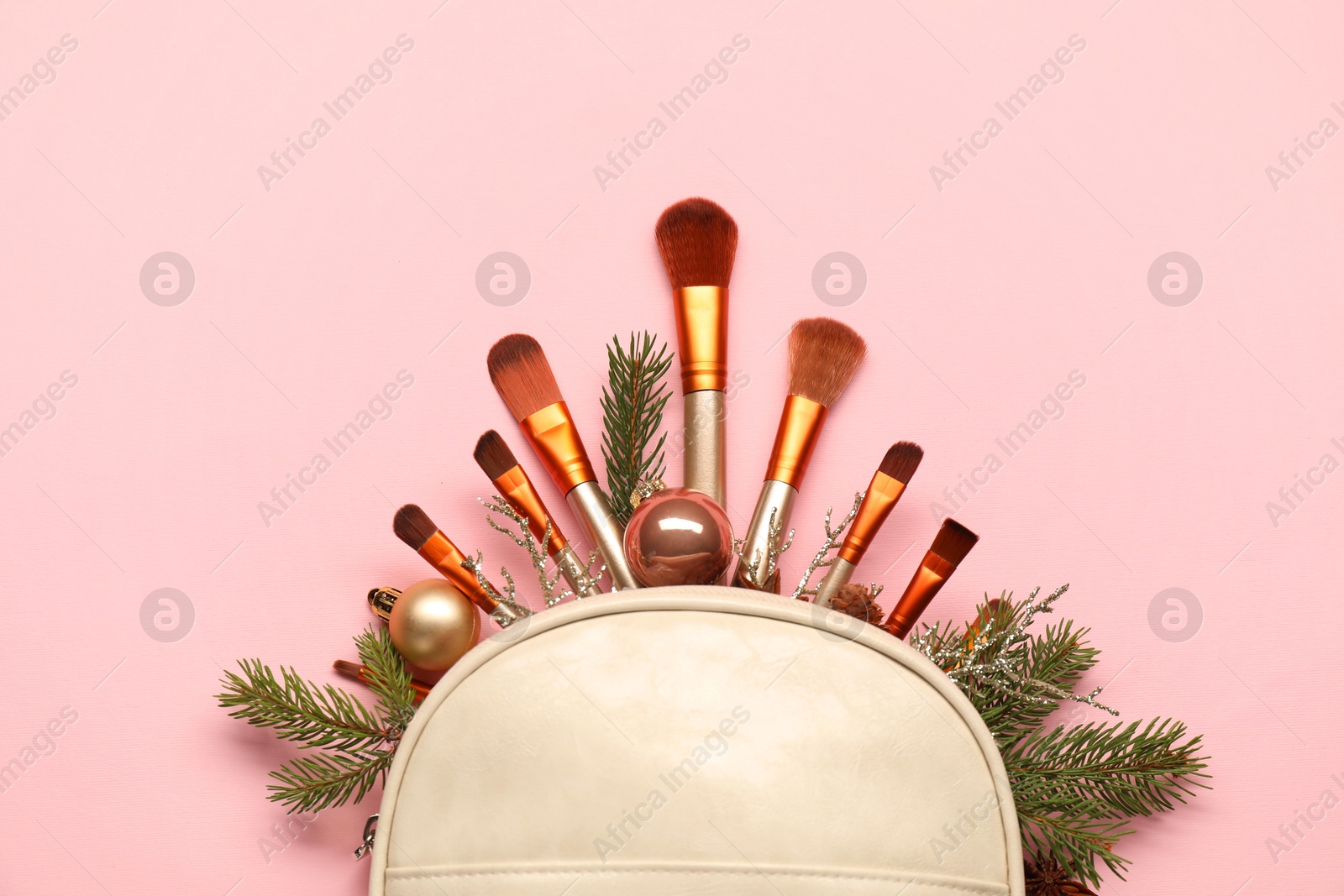 Photo of Cosmetic bag with makeup brushes and Christmas decor on pink background, top view