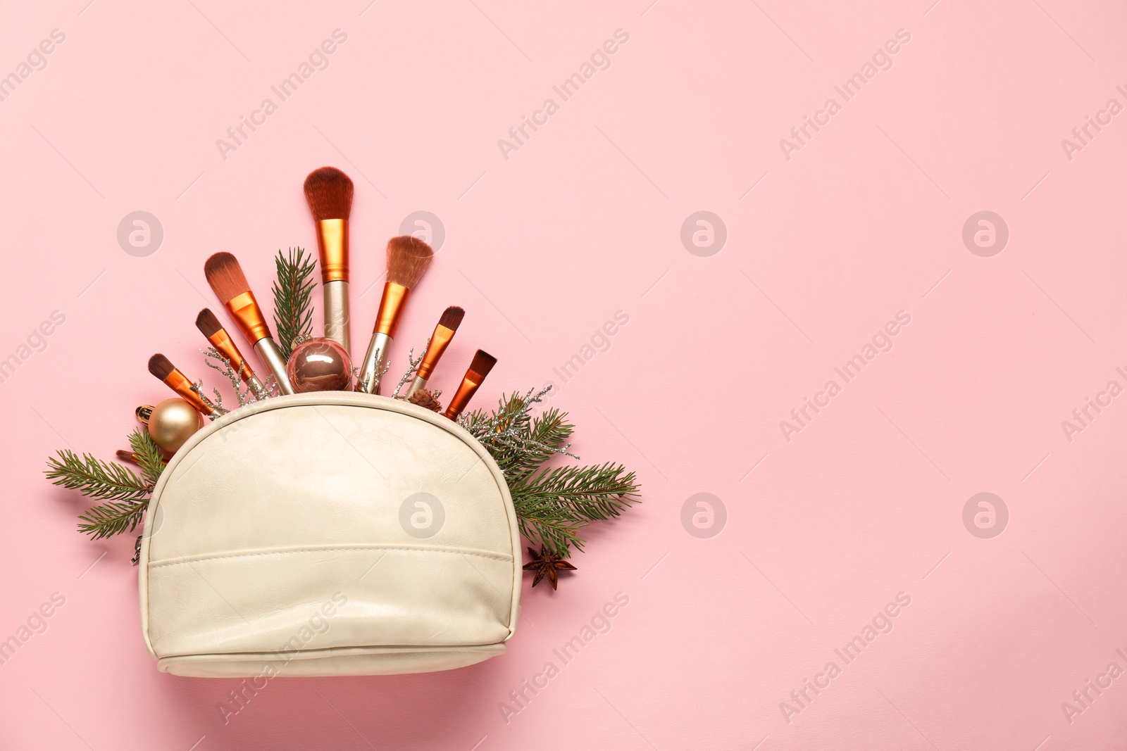 Photo of Cosmetic bag with makeup brushes and Christmas decor on pink background, top view. Space for text