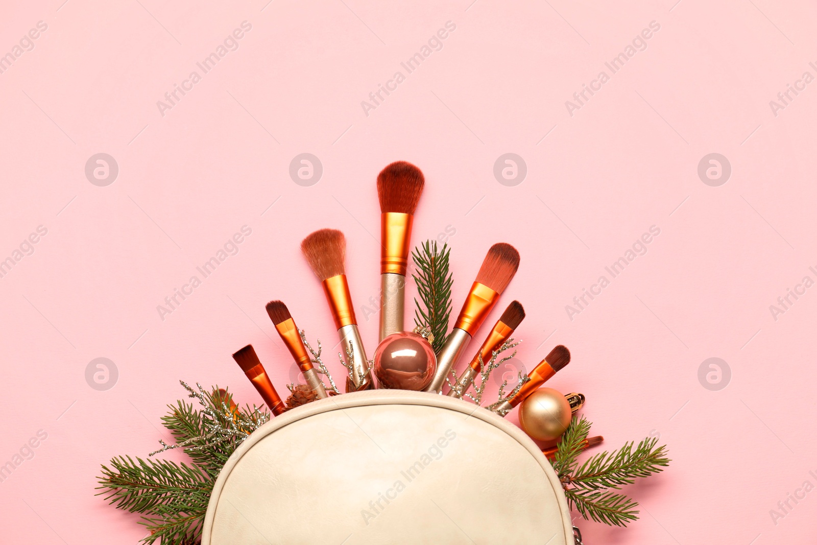 Photo of Cosmetic bag with makeup brushes and Christmas decor on pink background, top view