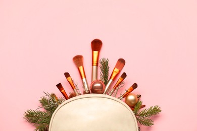 Photo of Cosmetic bag with makeup brushes and Christmas decor on pink background, top view