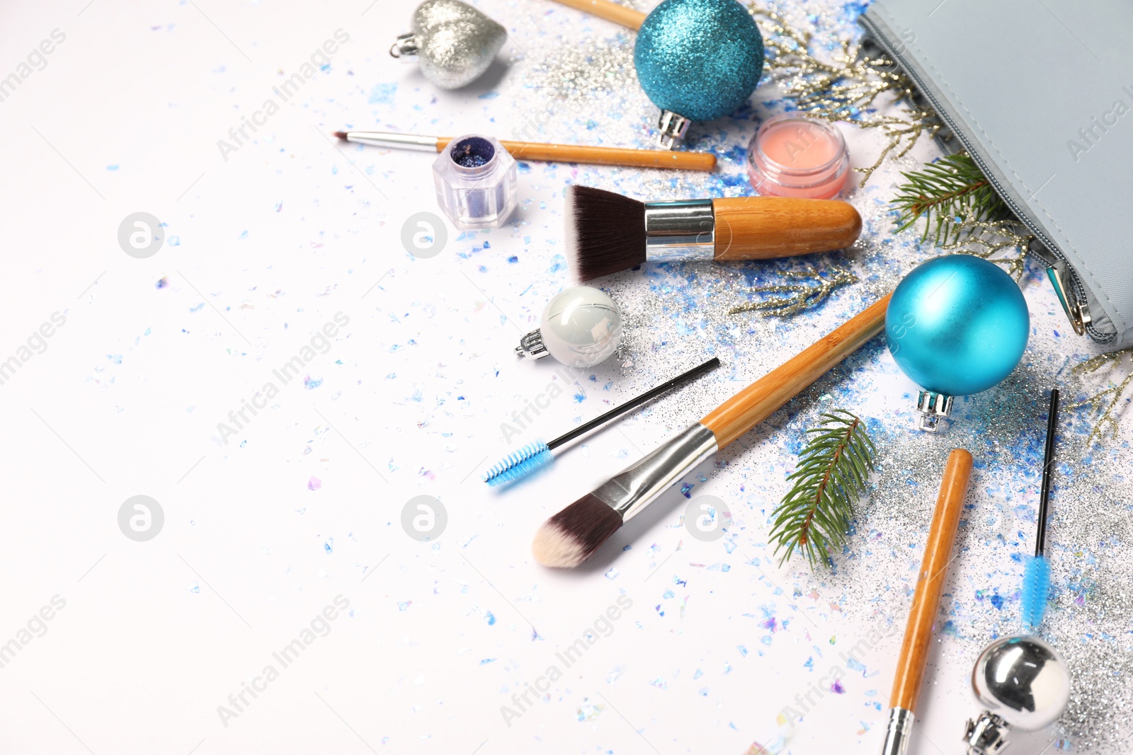 Photo of Cosmetic bag, makeup brushes, decorative cosmetics and Christmas decor on white background, flat lay. Space for text