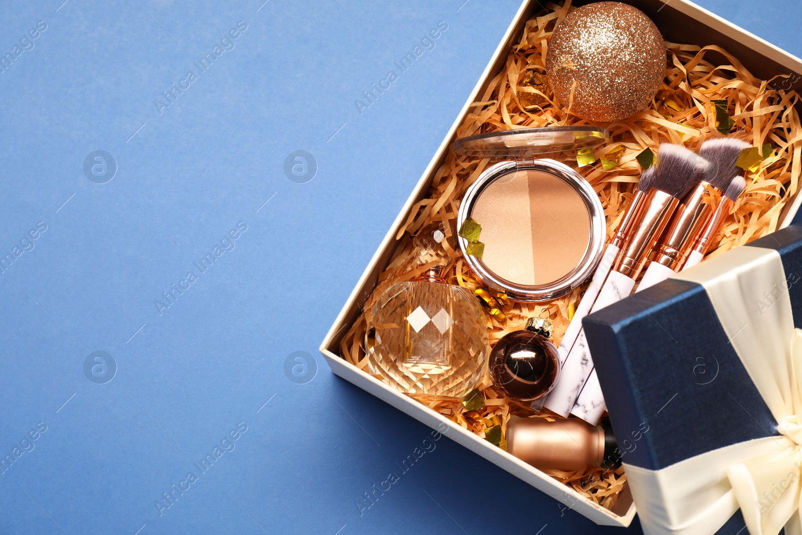 Photo of Makeup brushes, decorative cosmetics, perfume and Christmas decor in box on blue background, top view. Space for text