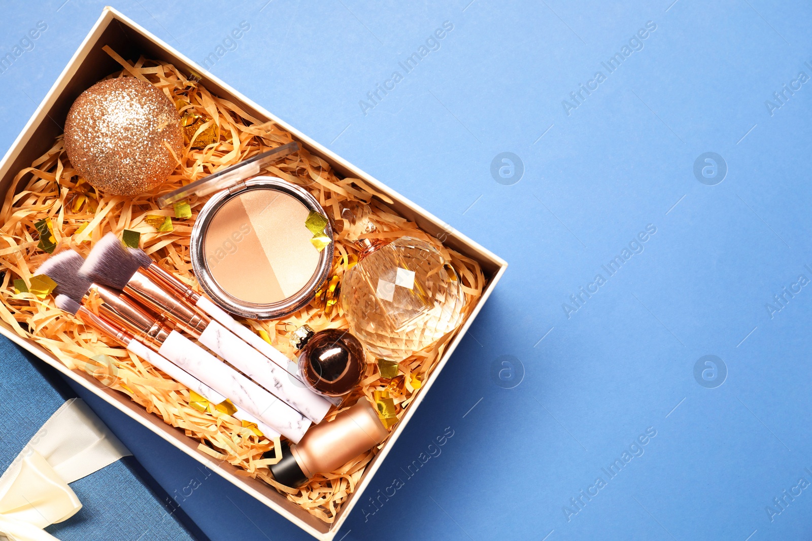 Photo of Makeup brushes, decorative cosmetics, perfume and Christmas decor in box on blue background, top view. Space for text