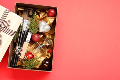 Photo of Makeup brushes, cosmetic product, perfume and Christmas decor in box on coral background, top view. Space for text