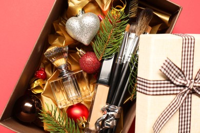 Photo of Makeup brushes, cosmetic product, perfume and Christmas decor in box on coral background, top view