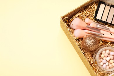 Photo of Makeup brushes, blush and Christmas decor in box on yellow background, above view. Space for text