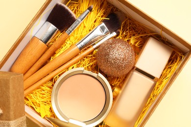 Photo of Makeup brushes, decorative cosmetics and Christmas decor in box on yellow background, top view