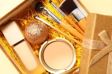 Photo of Makeup brushes, decorative cosmetics and Christmas decor in box on yellow background, top view