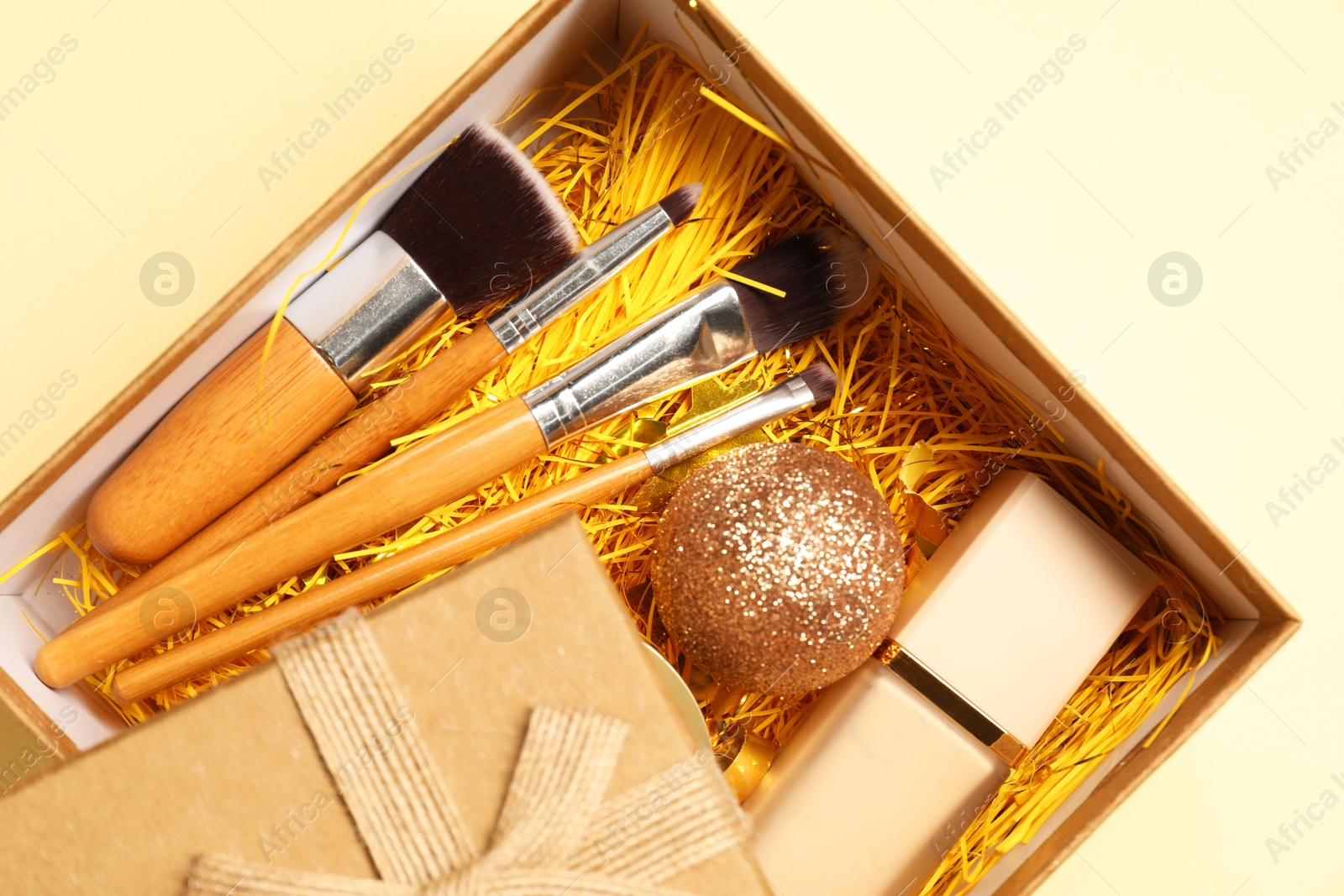 Photo of Makeup brushes, decorative cosmetics and Christmas decor in box on yellow background, top view