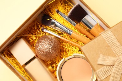 Photo of Makeup brushes, decorative cosmetics and Christmas decor in box on yellow background, top view