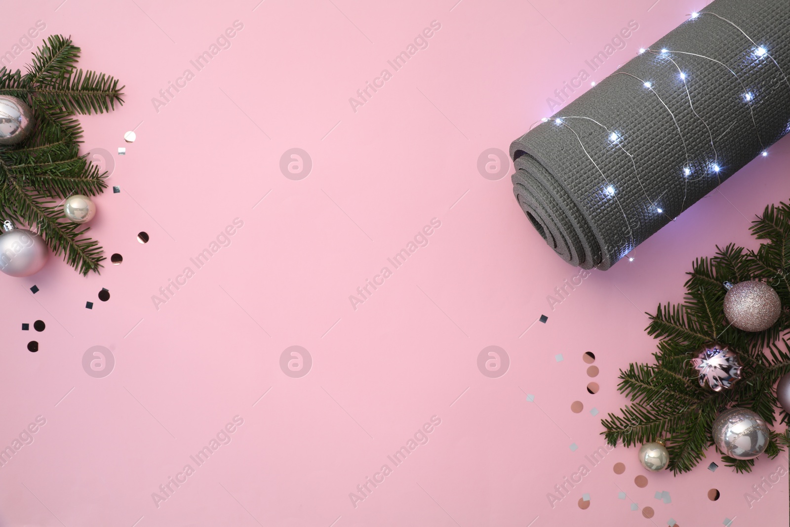 Photo of Yoga mat, baubles, fir branches and Christmas lights on pink background, flat lay. Space for text