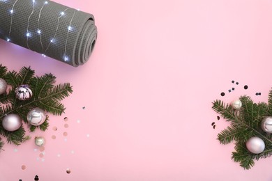 Photo of Yoga mat, baubles, fir branches and Christmas lights on pink background, flat lay. Space for text