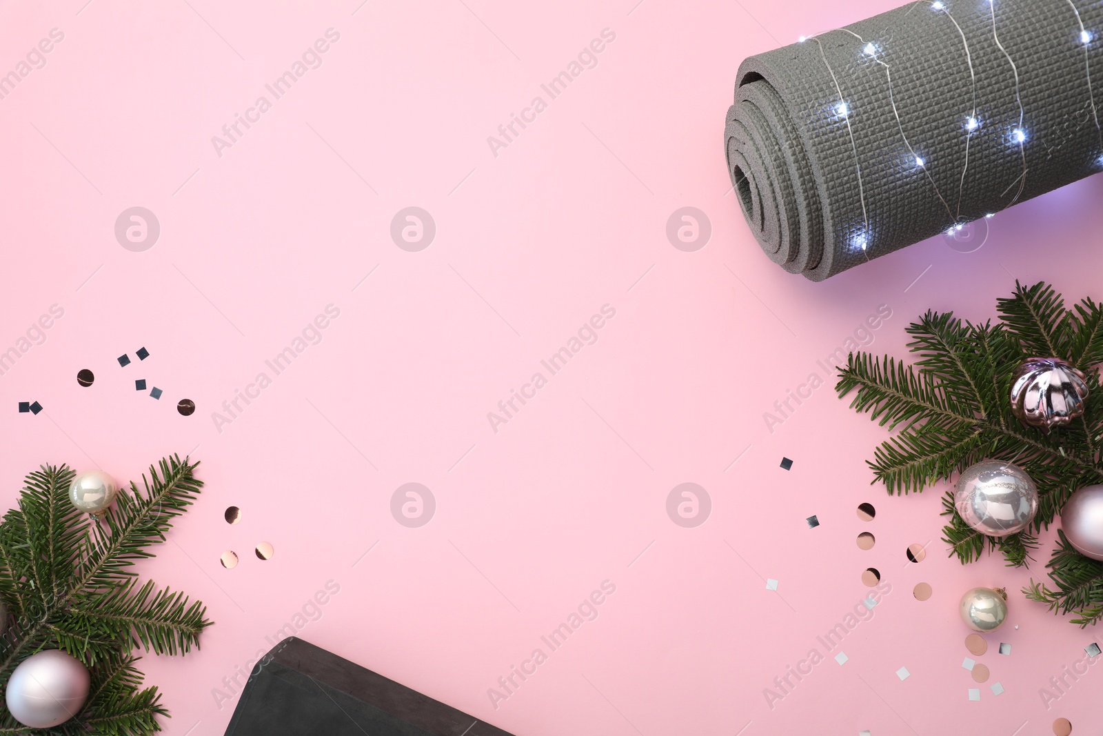 Photo of Yoga mat, baubles, fir branches and Christmas lights on pink background, flat lay. Space for text