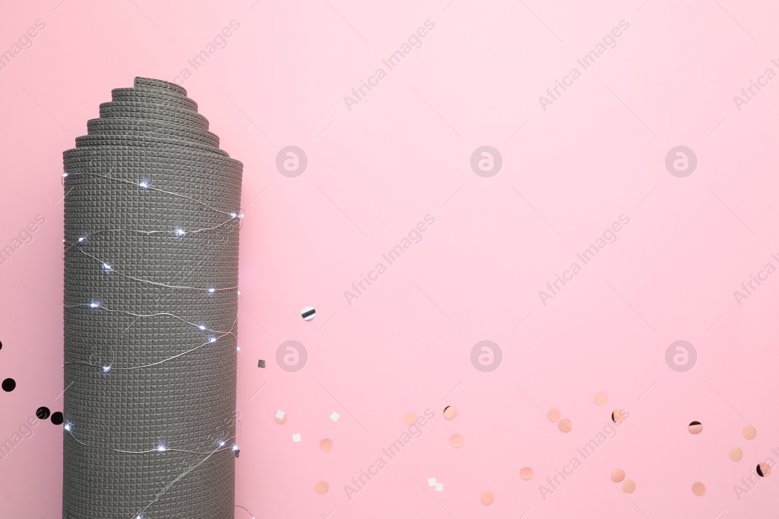 Photo of Yoga mat and Christmas lights on pink background, top view. Space for text