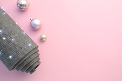 Photo of Yoga mat, baubles and Christmas lights on pink background, flat lay. Space for text