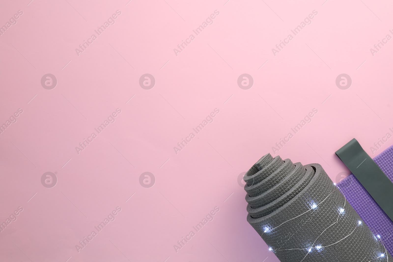 Photo of Yoga mat, block, elastic band and Christmas lights on pink background, flat lay. Space for text