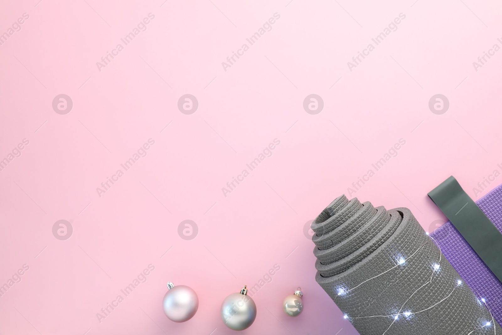 Photo of Yoga mat, block, elastic band and Christmas lights on pink background, flat lay. Space for text