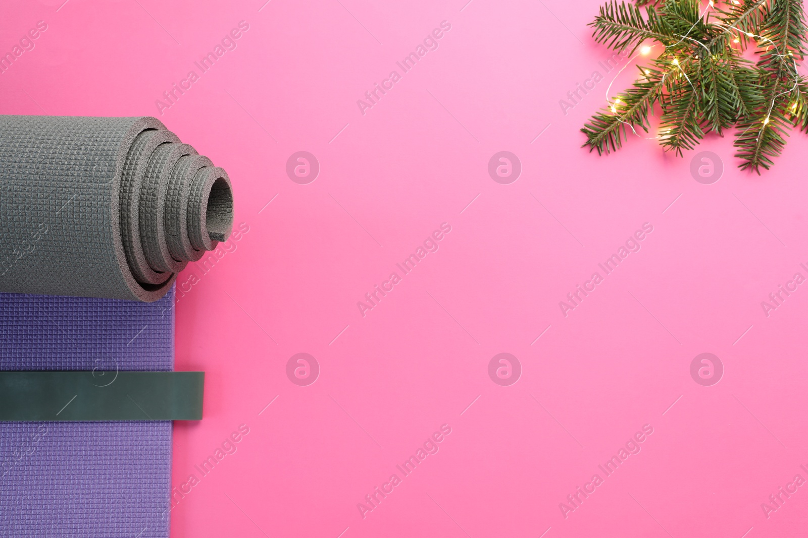 Photo of Yoga mat, elastic band, Christmas lights and fir branches on pink background, flat lay. Space for text