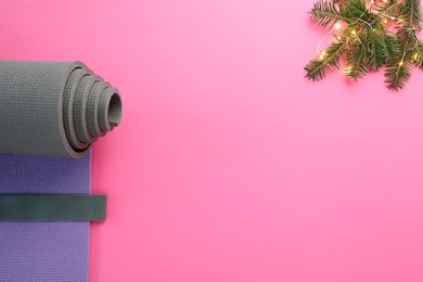 Photo of Yoga mat, elastic band, Christmas lights and fir branches on pink background, flat lay. Space for text