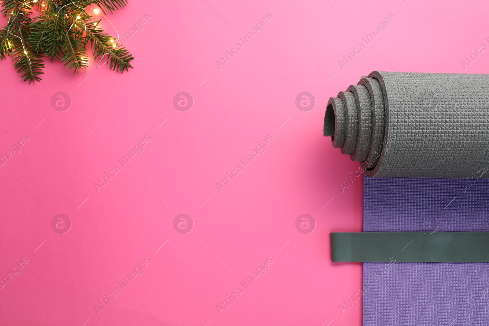 Photo of Yoga mat, elastic band, Christmas lights and fir branches on pink background, flat lay. Space for text